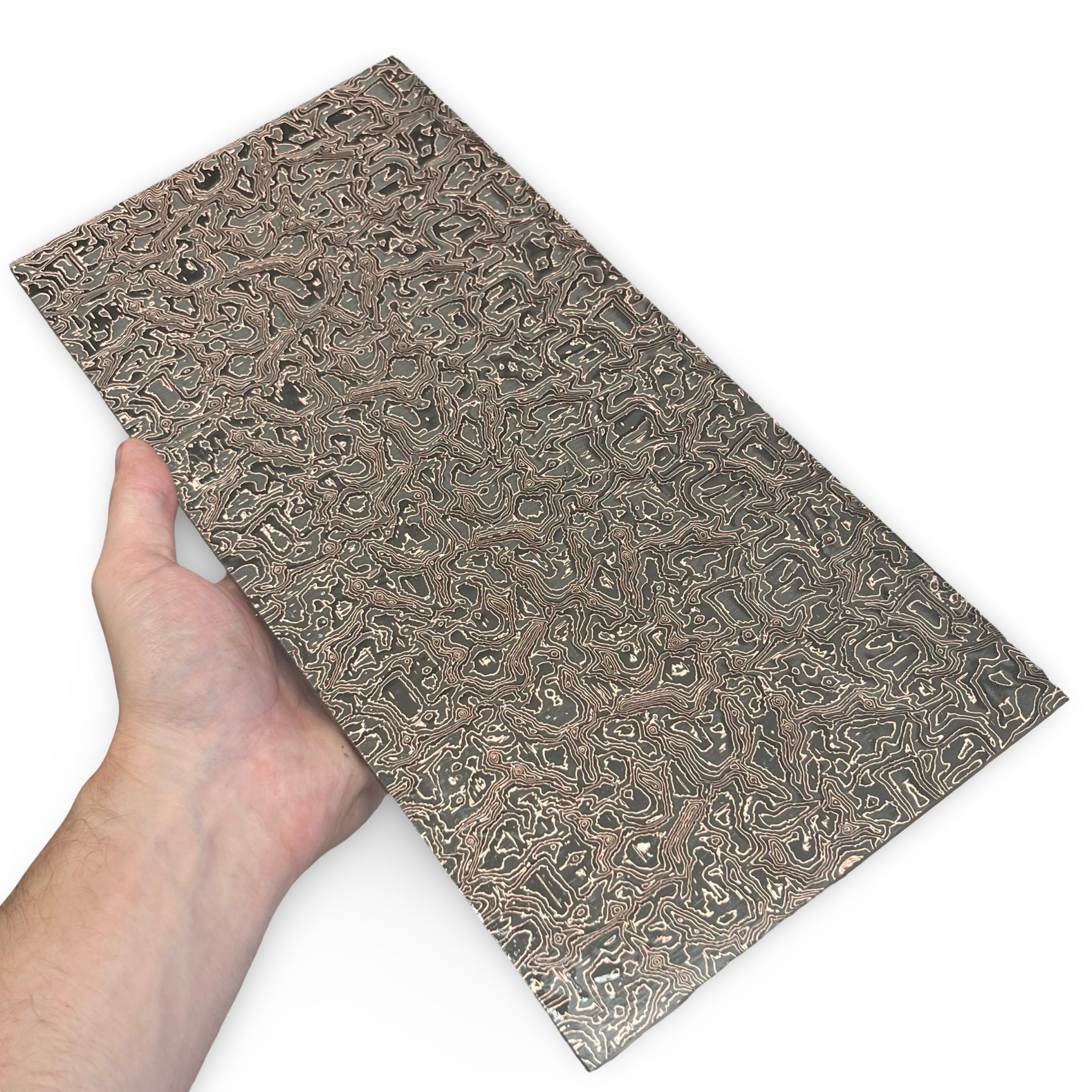 Hand holding a rectangular piece of Carbon fiber with intricate copper patterns on a white background